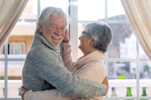 A beautiful couple of senior people hugging while dancing in front of the window. Two active retirees are having fun