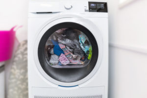Electric dryer with clothes inside in the laundry room