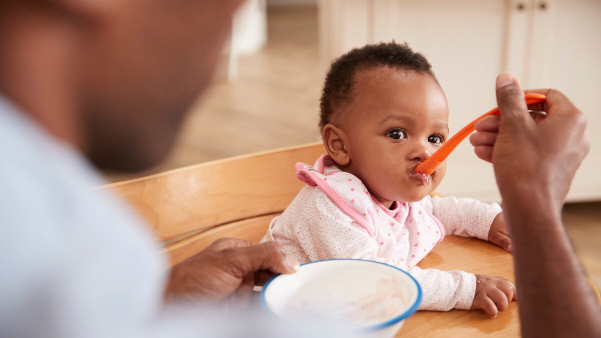 Father Feeding Baby Daughter In High Chair